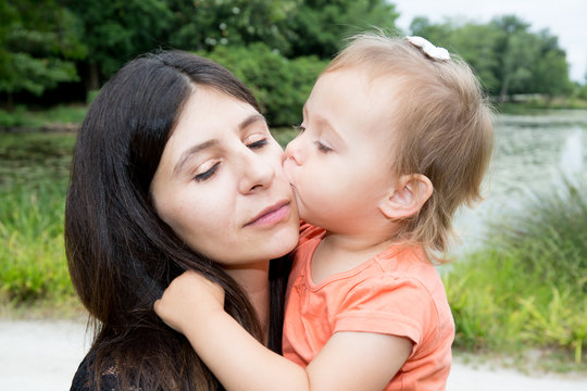 little girl daughter kiss cheerful mother in park near lake