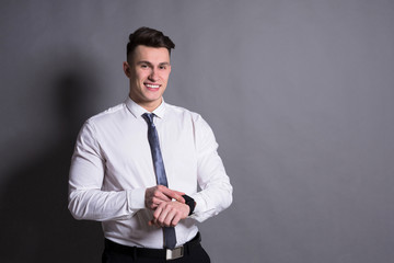 Confident youn businessman checking hand watch time on gray studio background