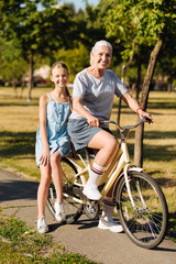 Positive senior woman riding her granddaughter on the bicycle