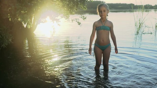 Cute little girl is splashes and catches soap bubbles standing in the water of a picturesque forest lake in the light of a glares on the water. Slow motion.