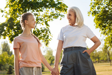 Cheerful senior woman and her granddaughter holding hands together