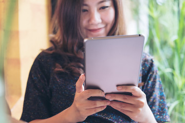 Fototapeta premium A beautiful Asian woman with smiley face holding , using and looking at tablet pc in modern cafe