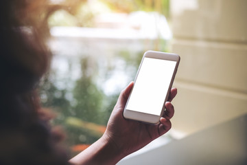 Mockup image of a woman holding and using white smart phone with blank screen with pond and nature background