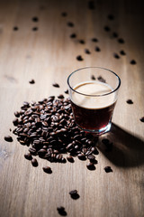 Fresh coffee in a glass with coffee beans on a wood table