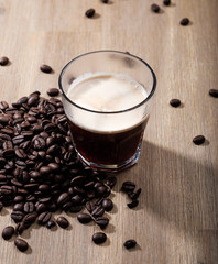 Fresh coffee in a glass with coffee beans on a wood table