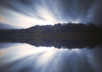 Reflection of mountains and clouds on a calm water.