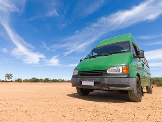 Fototapeta na wymiar A old green backpackers motorhome camper van, in the Australian outback, with a vivid blue sky and famous red dirt floor. The Australian outback is a great place for travellers.