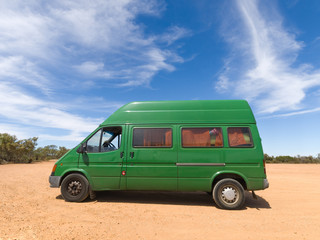 A old green backpackers motorhome camper van, in the Australian outback, with a vivid blue sky and...