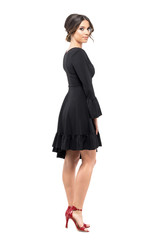 Beauty woman in black dress and red stiletto sandals turning and looking at camera. Full body length portrait isolated on white background.