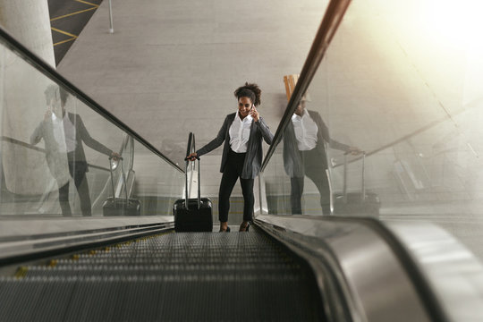 Businesswoman using escalator at airport terminal and holding smartphone