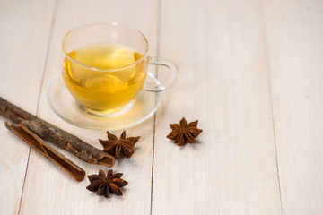 Cup of black tea with spices on white wooden background.