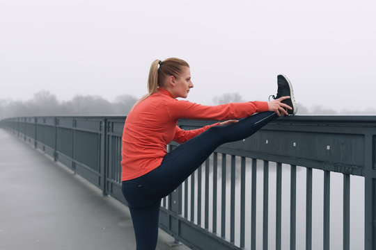 Läuferin beim Stretching bei Nebel auf einer Brücke in Magdeburg, Deutschland