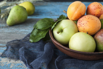 Apples, pears and apricots in a plate on a wooden table