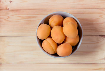 Bowl full of fresh apricots on wooden background. Top view.