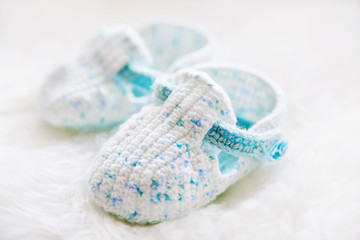 Little baby shoes. Handknitted first shoes for boy or girl. Crochet handmade bootees on white fluffy background.