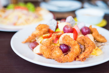 Fried shrimp with mixed fruit salad in white dish.