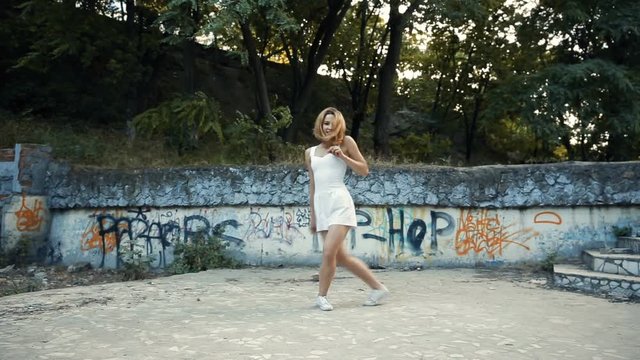Young Asian woman dancing modern choreography in city park, outside. City ruins and graffiti. Variety