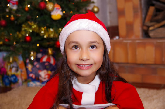 Beautiful smiling litle girl wearing a christmas clothes with a christmas tree background with some presents