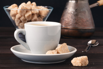 Cup of coffee with brown sugar on a light wooden table.
