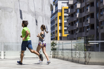 Handsome man and beautiful woman jogging together on street between residential buildings