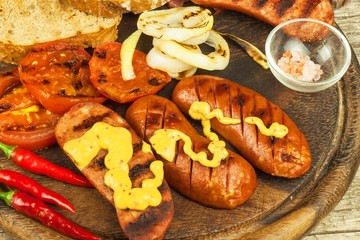 Grilled sausage with mustard on a wooden cutting board. Summer barbecue party. Fat meal.
