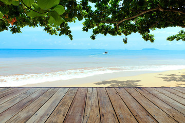 Top of the empty wooden floor under the shadow of the Indian almond tree on the sea-view background there is a boat, island and blue sky with clouds, product display concept