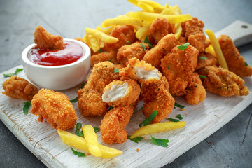 Fried crispy chicken nuggets with french fries and ketchup on white board