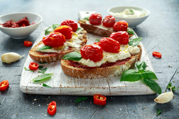 Tomato Ricotta Bruschetta with sun dried tomatoes paste, olive oil brown bread and basil in a white wooden board.