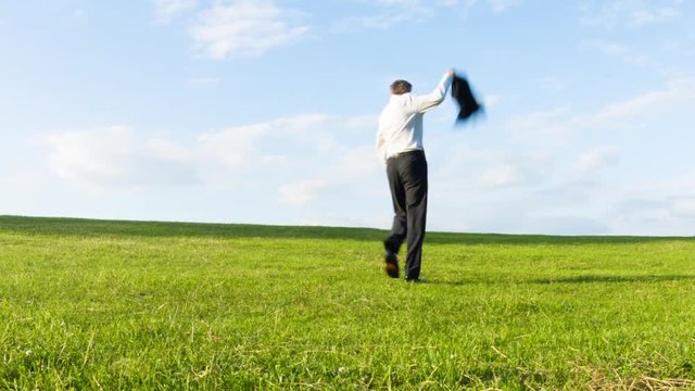 Carefree happy middle aged Caucasian businessman throwing off his jacket as he walks over a hill in celebration getting away from it all concept