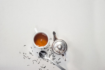 vintage white cup, a silver antique kettle, a spoon, a scattered dry tea on a gray background.