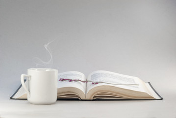 White vintage cup hot tea on the background of the book. Violet flowers herbarium bookmark