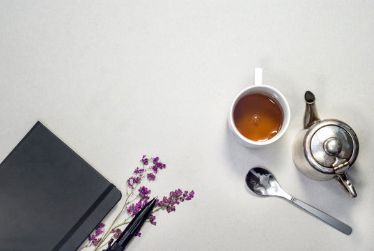 Silver teapot, white vintage cup, notebook, dry fiolet flowers handle on gray  background. Business concept