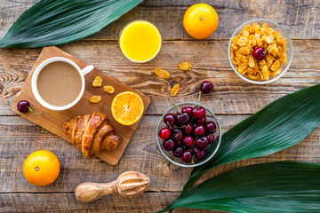 French breakfast. Fresh croissant, coffee, muesli, oranges, cherry on wooden table background top view