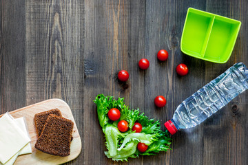 Heathy meal in office. Lunch box with vegetables, cheese and bread on dark wooden background top view copyspace
