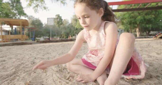 Little girl playing in a sandbox at the playground afternoon
