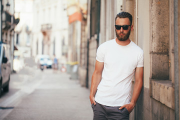 Hipster handsome male model with beard wearing white blank t-shirt with space for your logo or design in casual urban style - obrazy, fototapety, plakaty