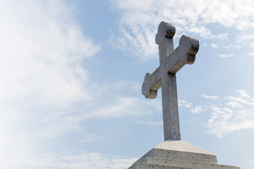 Christian stone cross on blue sky with clouds 