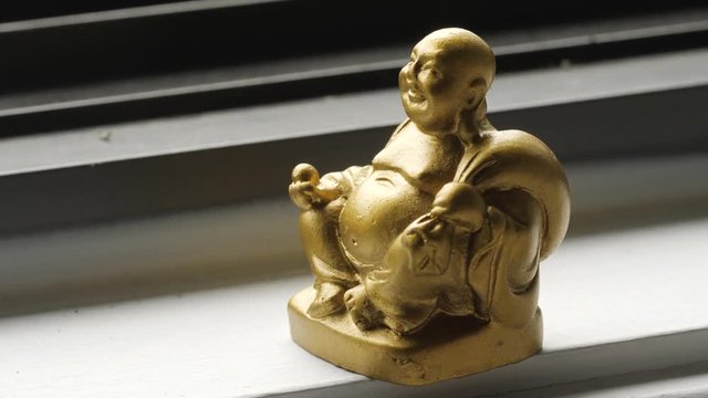 Close up of the hand placing golden Buddha statue near a window.