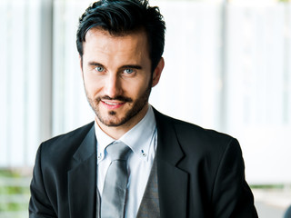 Portrait businessman smart confident and handsome with blue eyes and mustache in a formal attire or business suit and a grey necktie. He is in a relaxed period during an office montly meeting