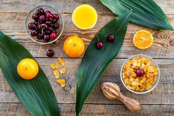 Summer fruity breakfast. Muesli, oranges, cherry on wooden table background top view