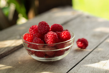 freshly harvested raspberries in a glass bowl on  rustic wooden table