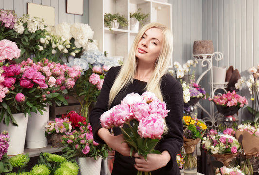Young woman holding beautiful peonies in flower shop