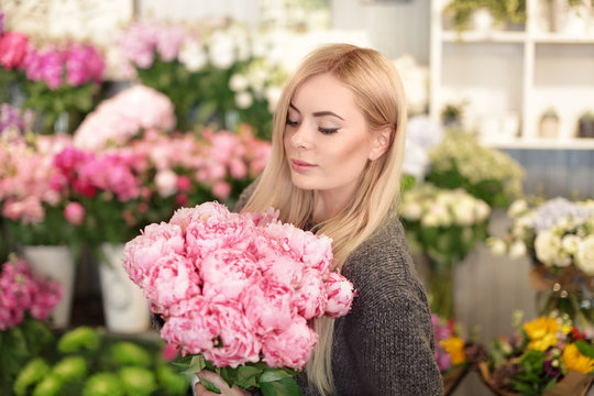 Young woman holding beautiful peonies in flower shop