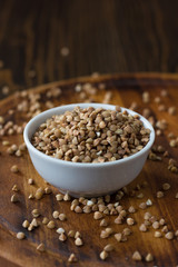 Buckwheat grain on ceramic bowl over wooden table.