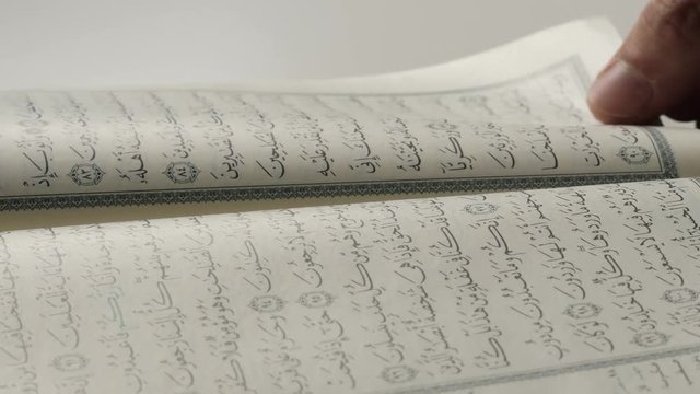 Hands turning the pages of the Quran reading and browsing the book. Closeup shot.
