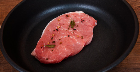 raw meat steak on cast iron frying pan on the brown wooden table background.