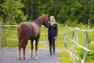 Young woman with her arabian horse standing at a riding course