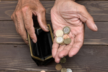 An elderly person holds the coins over the old empty wallet. The concept of poverty in retirement.