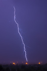 Naklejka premium Single lightning in stormy sky over field and street lights