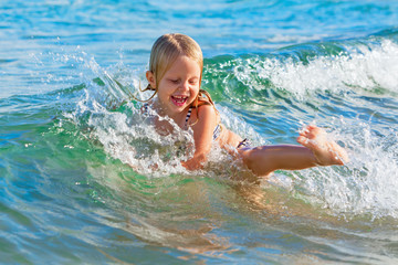 Fototapeta na wymiar Happy family lifestyle. Baby girl splashing and jumping with fun in breaking waves. Summer travel, water sport outdoor activities, swimming lessons on tropical beach holiday with kids.